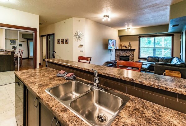 A kitchen with granite countertops, stainless steel sink, and a stone fireplace. - Pool, Hot Tub & Gym | Near Fernie Alpine Resort (Fernie)