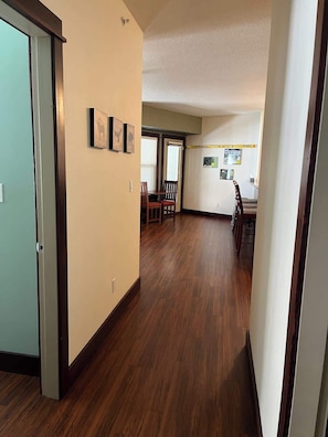 A hallway with wooden flooring, a dining area with chairs and a table, and a staircase leading to another level.