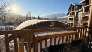 Una terraza de madera con una mesa y sillas, con vistas a un paisaje nevado y montañas distantes.