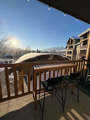 A wooden deck with a table and chairs, overlooking a snowy landscape with mountains in the distance.