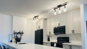 Una cocina moderna con armarios blancos, un refrigerador negro, una estufa y un microondas.