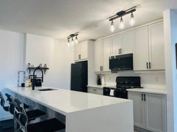 A modern kitchen with white cabinets, a black refrigerator, a stove, and a microwave.