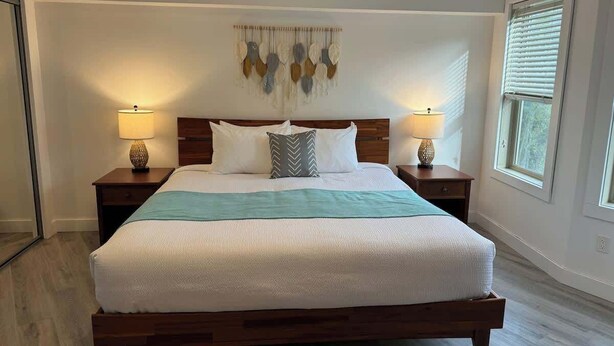 Un dormitorio amplio con una cama grande, cabecera de madera, dos mesitas de noche con lámparas y un adorno en la pared.