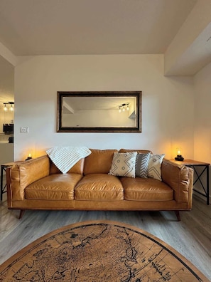 A brown leather sofa with patterned cushions, a large mirror above it, and a vintage-style world map rug on the floor.