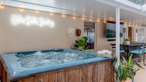 A hot tub with a wooden enclosure, a neon sign reading "Silver Dollar Spa," string lights, and a patio area with chairs and a table. - Private Spa/Heated Pool! Firepit, Pool/Game Tables-Near Crystal & Rainbow Rivers (Citrus Springs)
