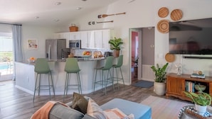 A modern kitchen with a central island, bar stools, and a dining area with a sofa. - Private Spa/Heated Pool! Firepit, Pool/Game Tables-Near Crystal & Rainbow Rivers (Citrus Springs)