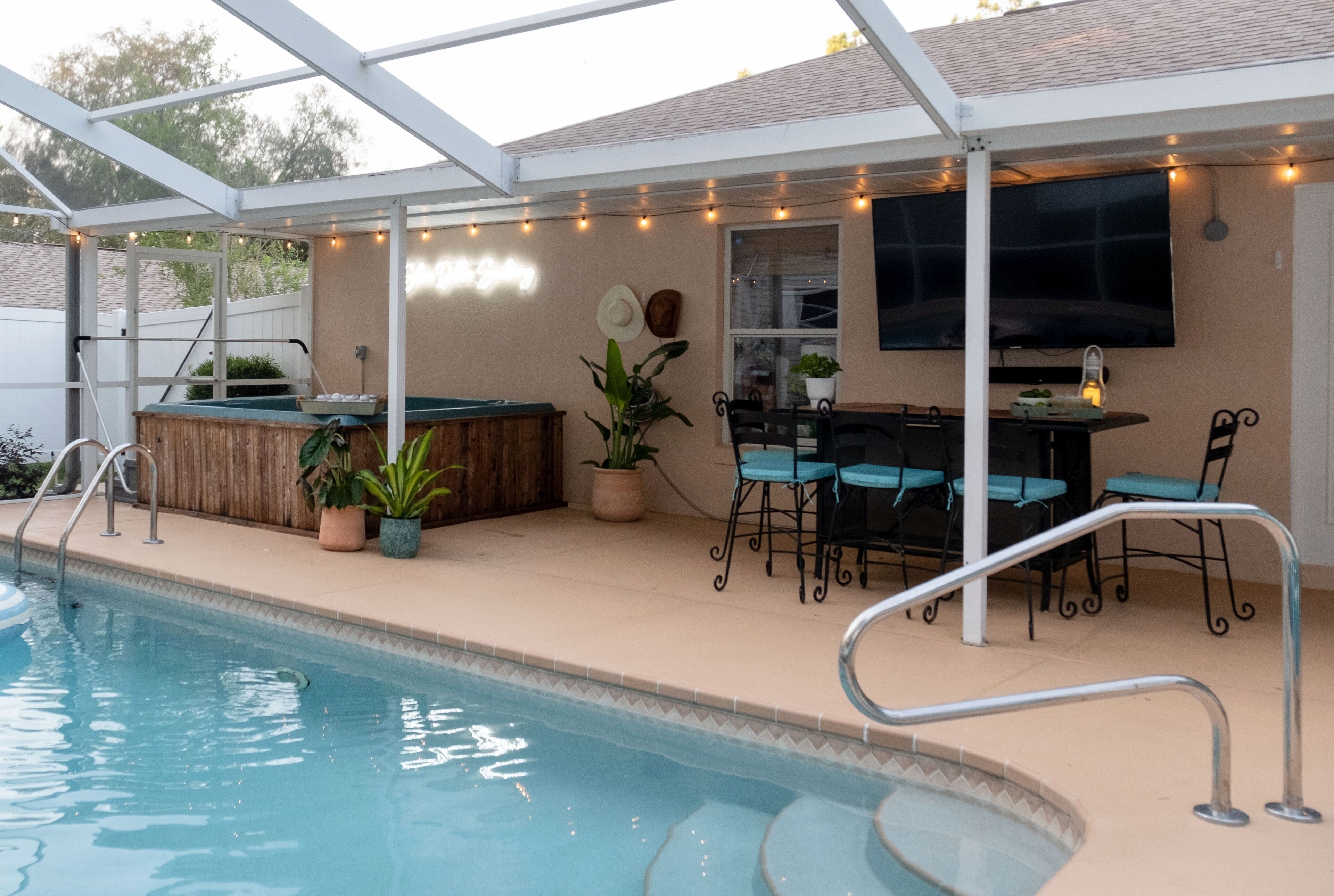 A covered outdoor pool area with a barbecue setup, seating, and string lights.
