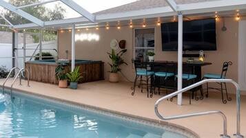 A covered outdoor pool area with a barbecue setup, seating, and string lights.