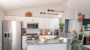 A modern kitchen with white cabinets, stainless steel appliances, a granite countertop, and a small island with bar stools. - Private Spa/Heated Pool! Firepit, Pool/Game Tables-Near Crystal & Rainbow Rivers (Citrus Springs)