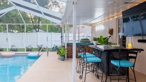 An outdoor pool area with a covered patio, bar with stools, and a TV mounted on the wall. - Private Spa/Heated Pool! Firepit, Pool/Game Tables-Near Crystal & Rainbow Rivers (Citrus Springs)