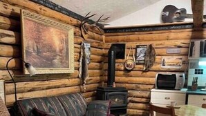 Une chambre aménagée dans un chalet en rondins, avec un lit, un canapé, une cheminée, un tableau et un coin repas.