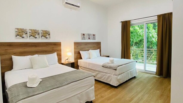 Ein Hotelzimmer mit zwei Betten, Holzboden, einem großen Fenster mit Vorhängen und einer Klimaanlage in der Decke.