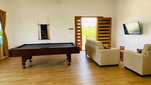 Ein modernes Wohnzimmer mit Billardtisch, einer Couch, einem Fernseher und einer Schiebetür, die auf einen Balkon führt.