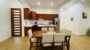 A modern kitchen with wooden cabinets, a stainless steel refrigerator, and a dining area with a wooden table and white chairs.