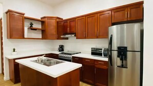 A modern kitchen with wooden cabinets, a stainless steel refrigerator, a sink, and a small trash bin.
