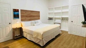 A bedroom with a large bed, white walls, wooden flooring, and built-in shelving.
