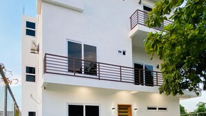 A modern two-story house with a balcony, a front door, and a small garden area with artificial grass and gravel pathways.