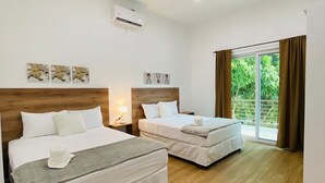 A hotel room with two beds, a wooden floor, a large window with curtains, and wall-mounted air conditioning. - Casa Victoria 1 (Flores)