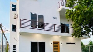 A modern two-story building with a balcony, a wooden door, and a well-maintained lawn. - Casa Victoria 1 (Flores)