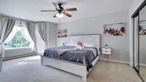 Une chambre à coucher avec un lit, un ventilateur de plafond, une table de chevet et une fenêtre avec des rideaux.