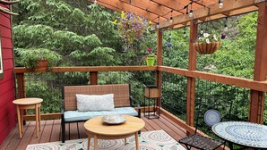 Une terrasse en bois avec un canapé en osier, une table ronde et une petite table ronde accompagnée de chaises.