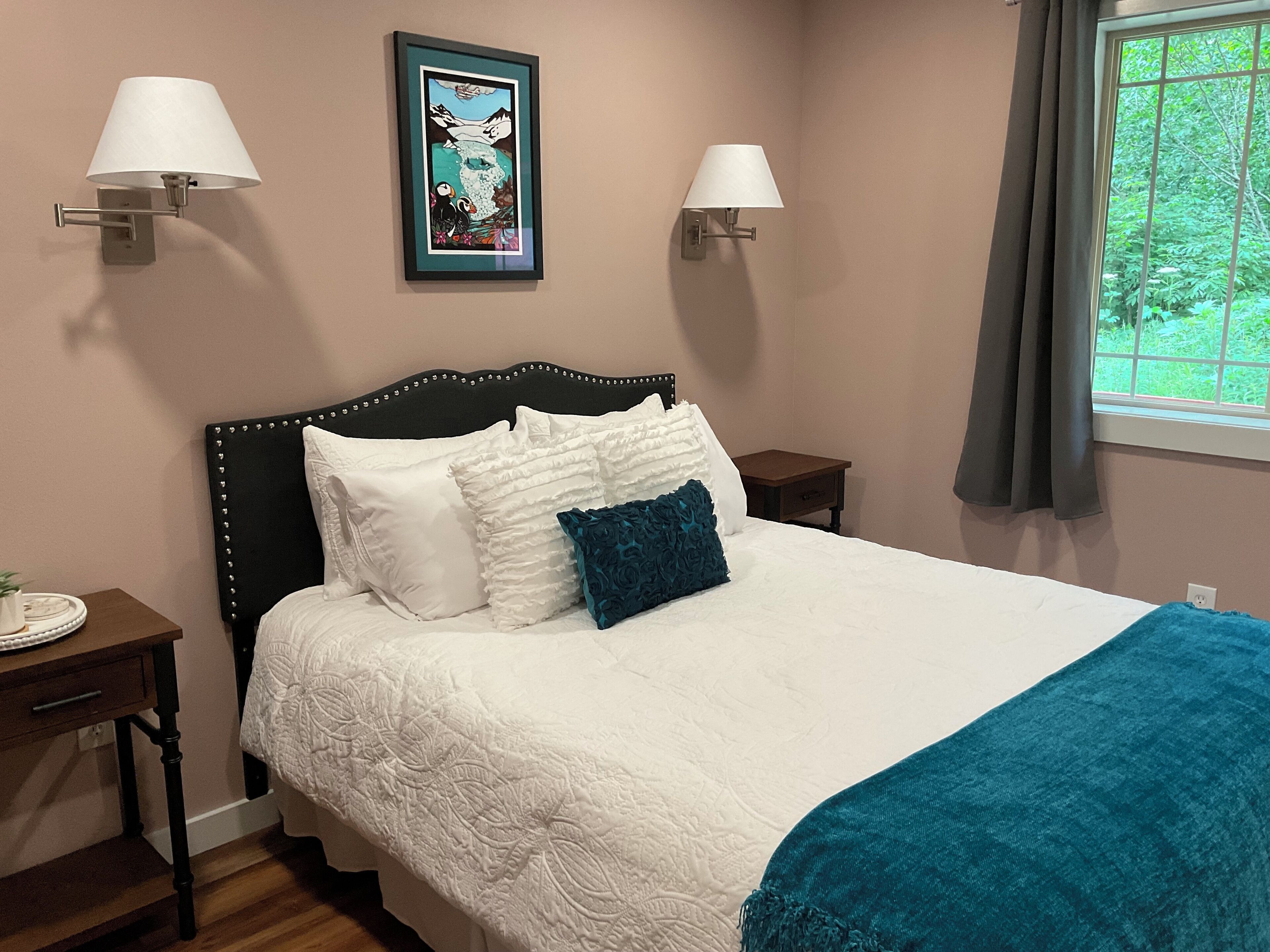 A neatly made bed with white and teal bedding, two wall-mounted lamps, and a framed picture above the headboard.