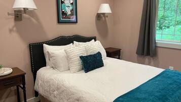 A neatly made bed with white and teal bedding, two wall-mounted lamps, and a framed picture above the headboard.
