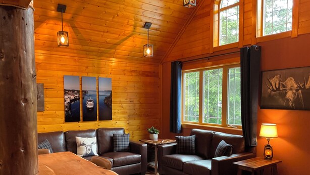 L’intérieur d’un chalet accueillant, avec des murs en bois, une table à manger en bois, deux canapés en cuir et une grande fenêtre agrémentée de rideaux.