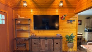 L’intérieur chaleureux d’un chalet avec un mur en bois, un téléviseur à écran plat, un meuble en bois et un coin repas.
