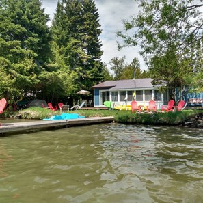 A lakeside cabin with a dock, surrounded by trees and equipped with outdoor seating and a small boat. - Little Lake Cottage (cra)