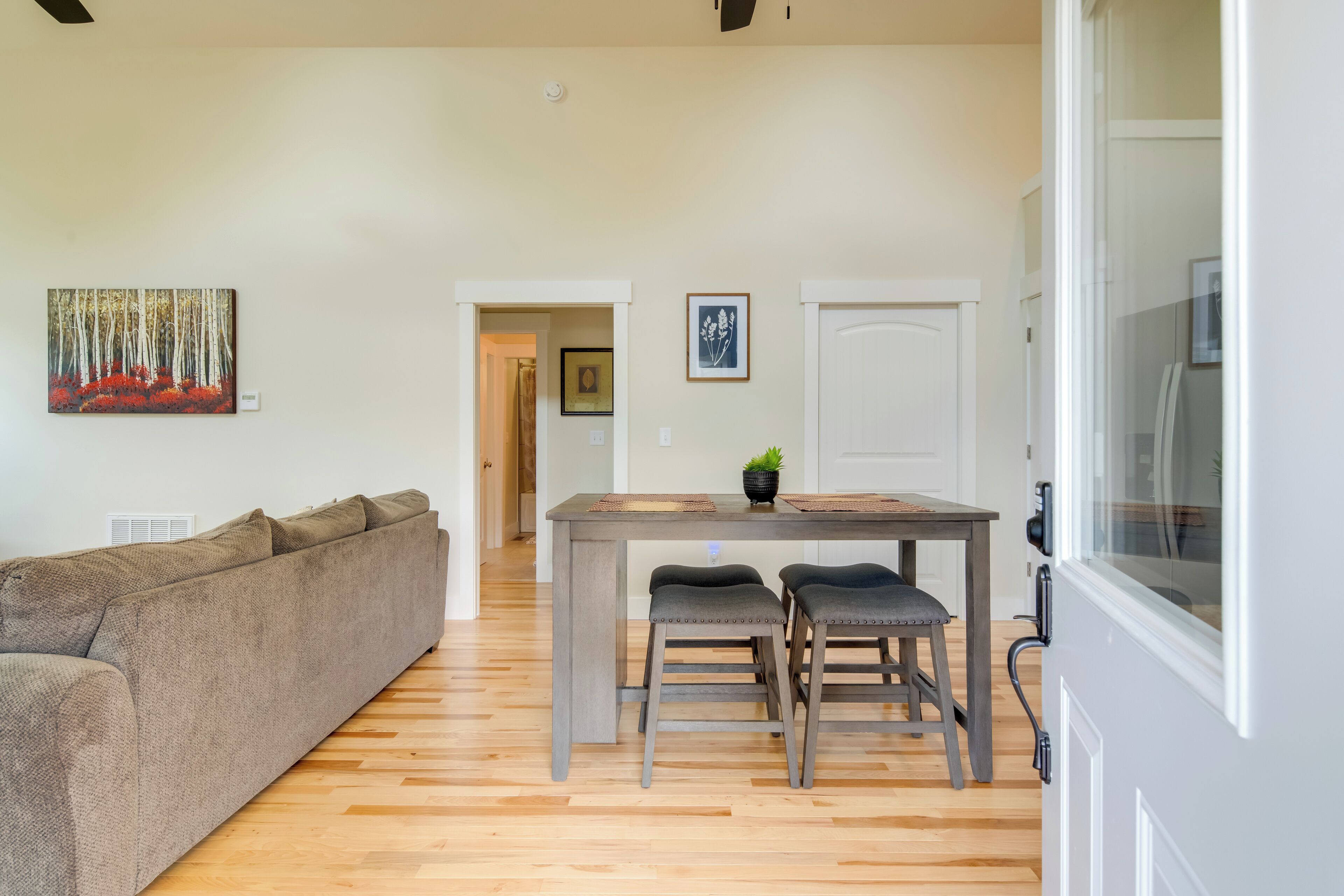 A living room with a sofa, a dining table with two chairs, and a painting on the wall.