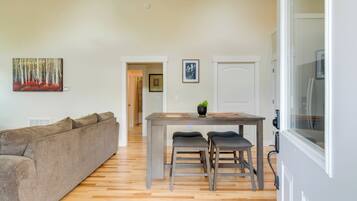 A living room with a sofa, a dining table with two chairs, and a painting on the wall.