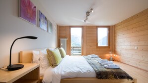 Une chambre avec un lit en bois, une table de chevet, un radiateur et une fenêtre donnant sur la montagne.