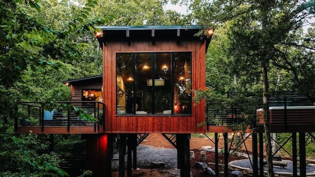 A wooden treehouse with a glass window, surrounded by dense forest.