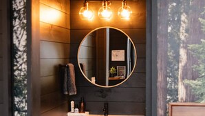 A bathroom with a wooden vanity, a round mirror, and three wall-mounted lights.