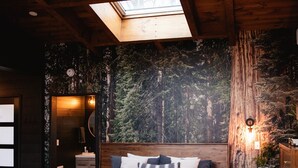 A bedroom with a skylight, a bed with pillows, a nightstand, and a wall with a forest mural.