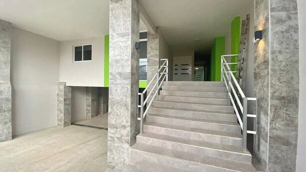A staircase with marble steps and metal railings, leading to a room with a green accent wall and a small window.