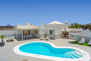 Un espace piscine comprenant une piscine, des chaises longues, un barbecue et un bâtiment équipé d’une antenne parabolique.