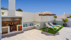 Een terras met een barbecue, twee lounge fauteuils, een kleine tuin en een witte muur.