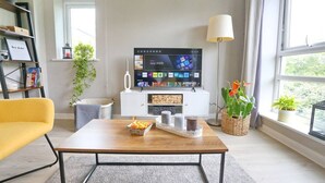 Ein modernes Wohnzimmer mit einem Flachbildfernseher, einem Couchtisch, einem gelben Sessel und einem großen Fenster mit Blick.