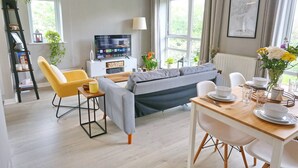 Ein modernes Wohnzimmer mit einer Couch, einem gelben Sessel, einem Esstisch und einem Fernseher.