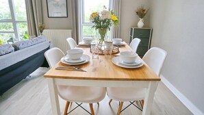 Ein Essbereich mit einem Holztisch, gedeckt für vier Personen, weißen Stühlen und einer Blumenvase.