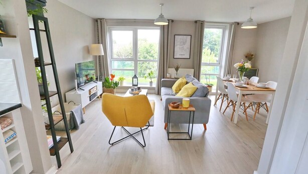 Ein modernes Wohnzimmer mit einer Couch, einem gelben Sessel, einem Esstisch und einem Fernseher.