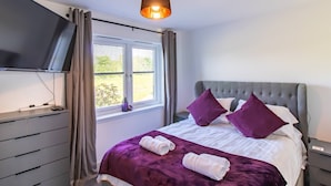 Quarto com cama, televisão, janela com cortinas e mesa de cabeceira.