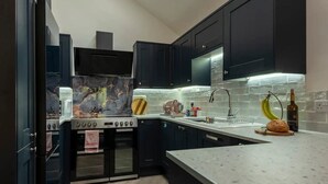 Une cuisine moderne avec des meubles de couleur sombre, une cuisinière en acier inoxydable et un dosseret en marbre.