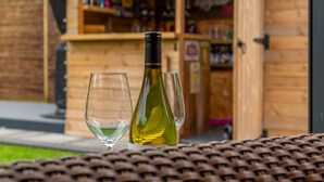 Une table en osier, avec deux verres à vin et une bouteille de vin blanc, dans un cadre extérieur.
