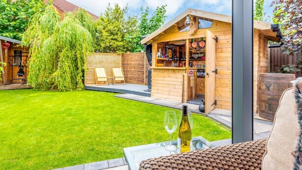 Un bar en bois avec des places assises à l’extérieur, une cour arrière verdoyante et une vue sur le ciel.