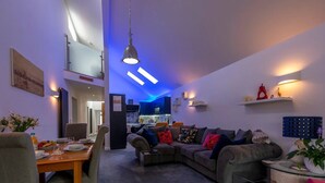 Un salon moderne avec un coin repas, une cuisine à l’arrière-plan et un escalier menant à un niveau supérieur.