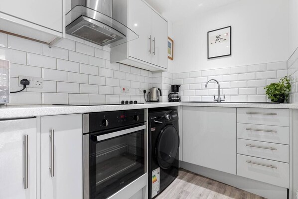 A modern kitchen with white cabinetry, a built-in oven, a washing machine, and a stainless steel range hood.