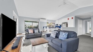 A modern living room with a grey sofa, a wooden coffee table, and a flat-screen TV. - Tura Beach Getaway on Telopea (Tura Beach)